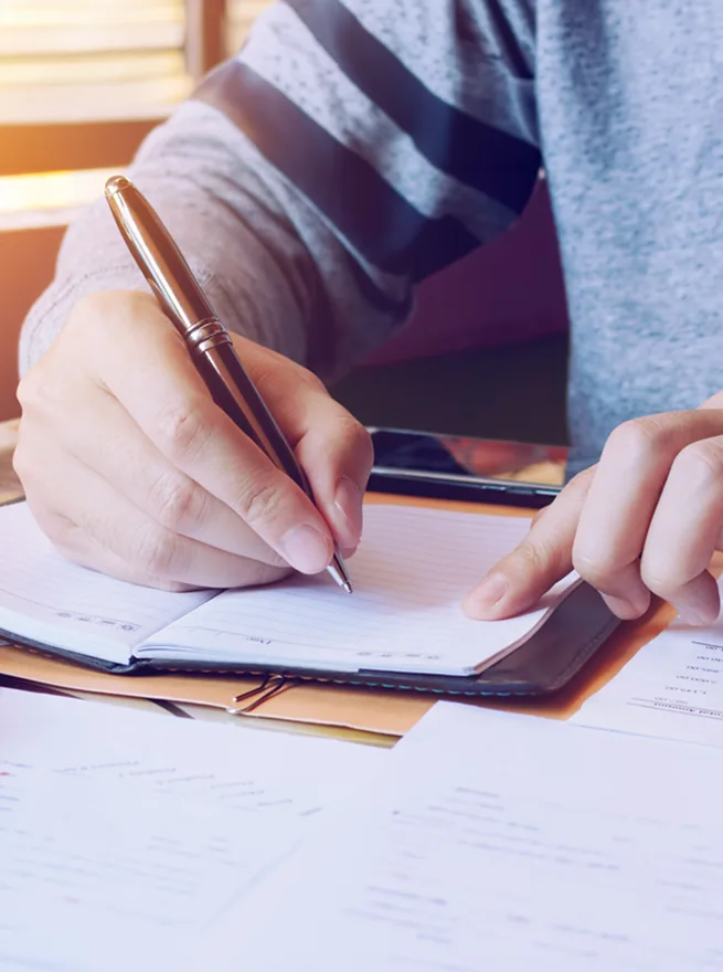 up close shot of a person writing on a pile of papers and notebook
