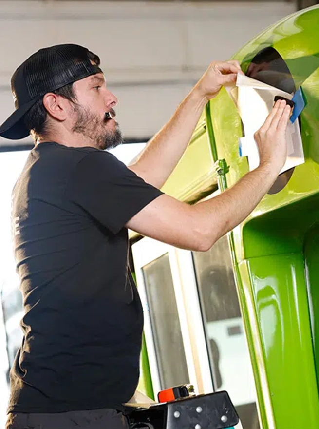 A Model 1 employee applying a graphic wrap onto a green vehicle